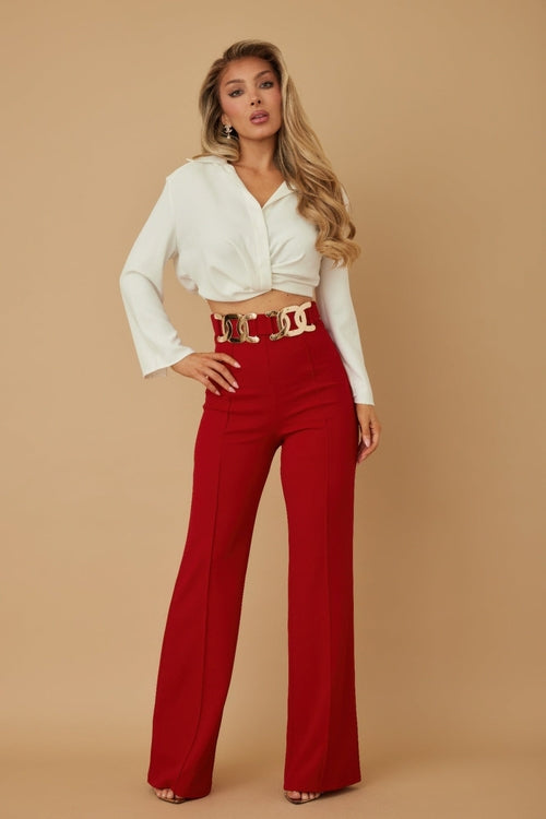 Woman wearing a white blouse and red pants with a gold belt on a beige background
